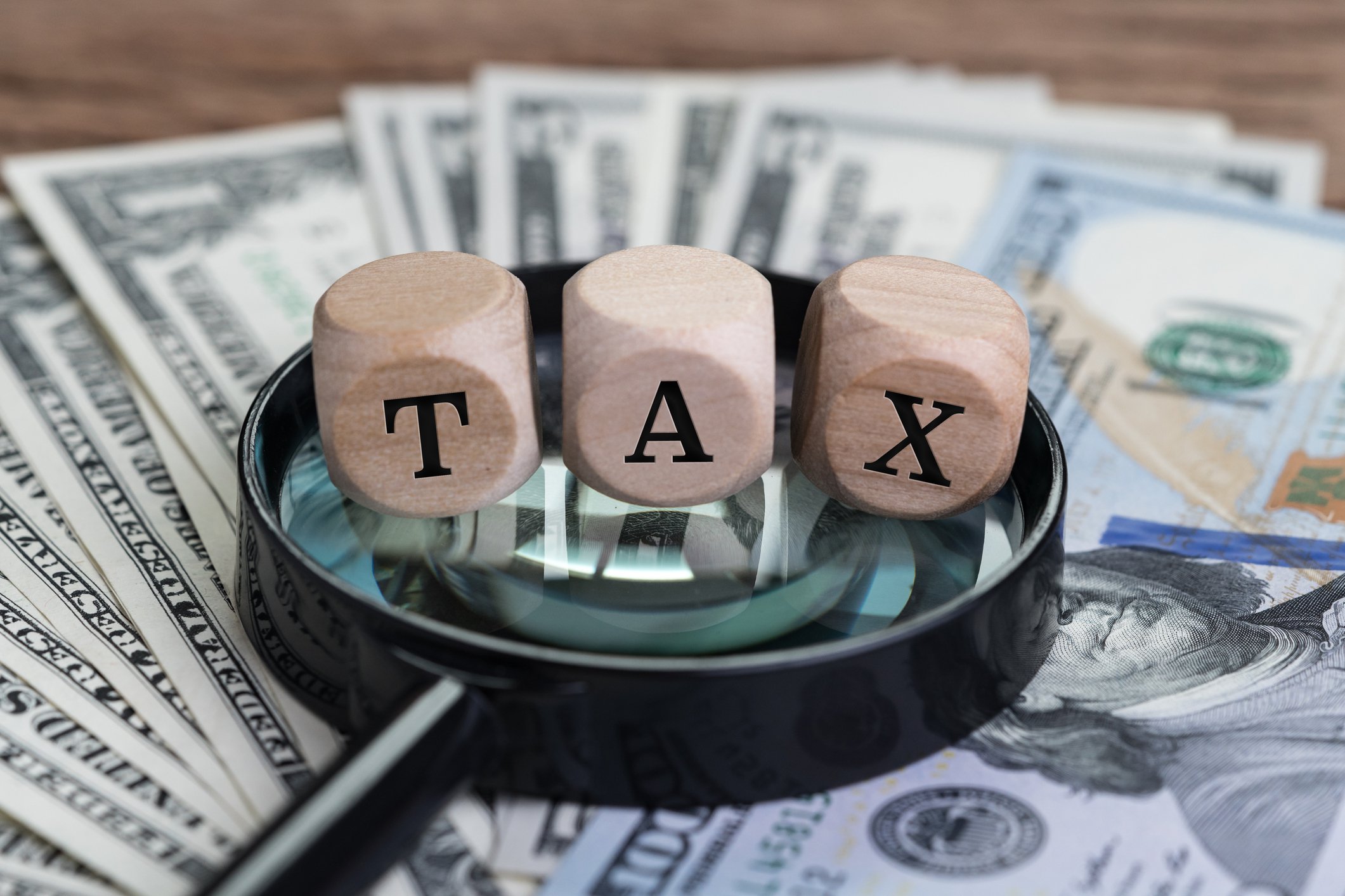 Blocks spelling TAX on top of a magnifying glass and pile of money.