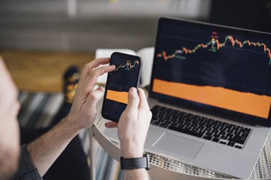 Man holding a phone showing same stock market chart as laptop.