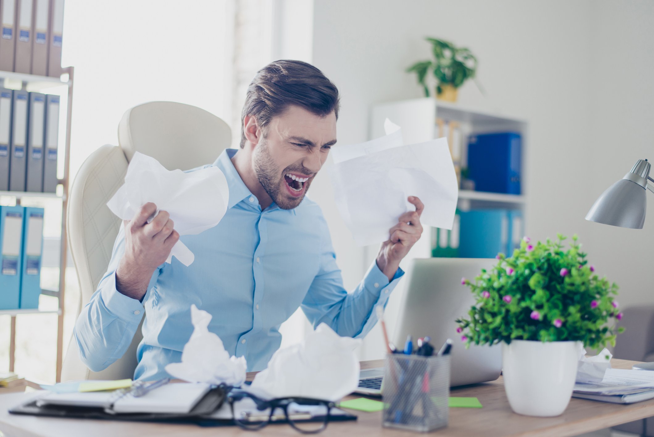 Angry man holding papers and screaming at laptop