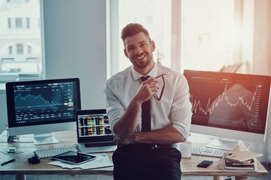 Man raises arms in success in front of computers