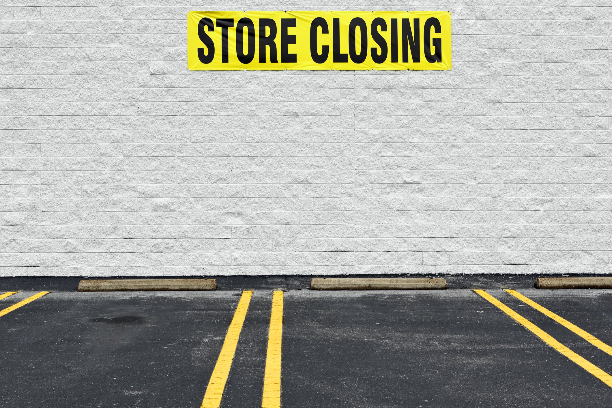 Bright yellow STORE CLOSING sign on a concrete wall.