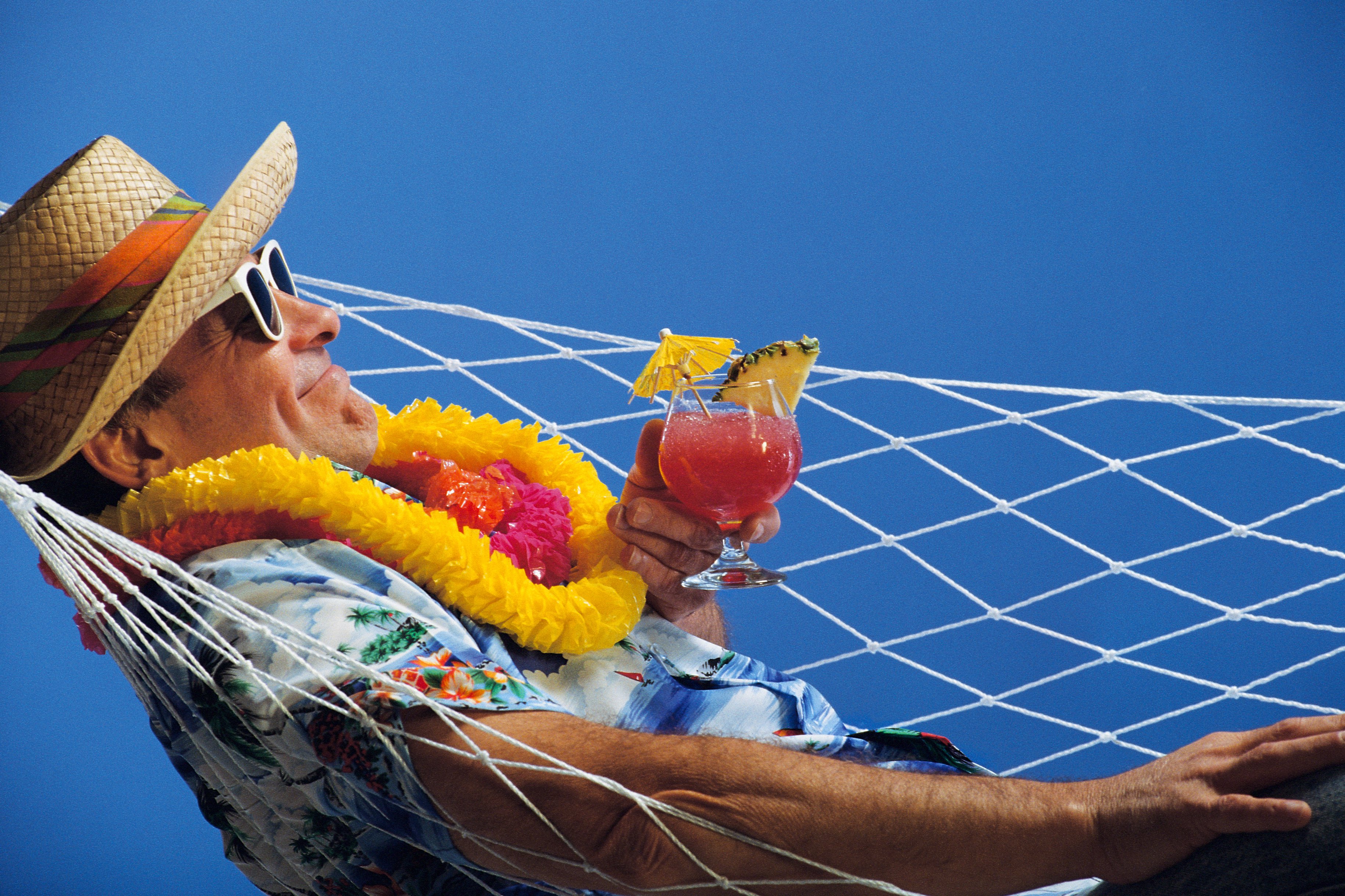 Mature man in a sun hat and lei lying in a hammock with drink