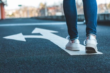 Pedestrian walking on road sign showing arrows pointing in different directions