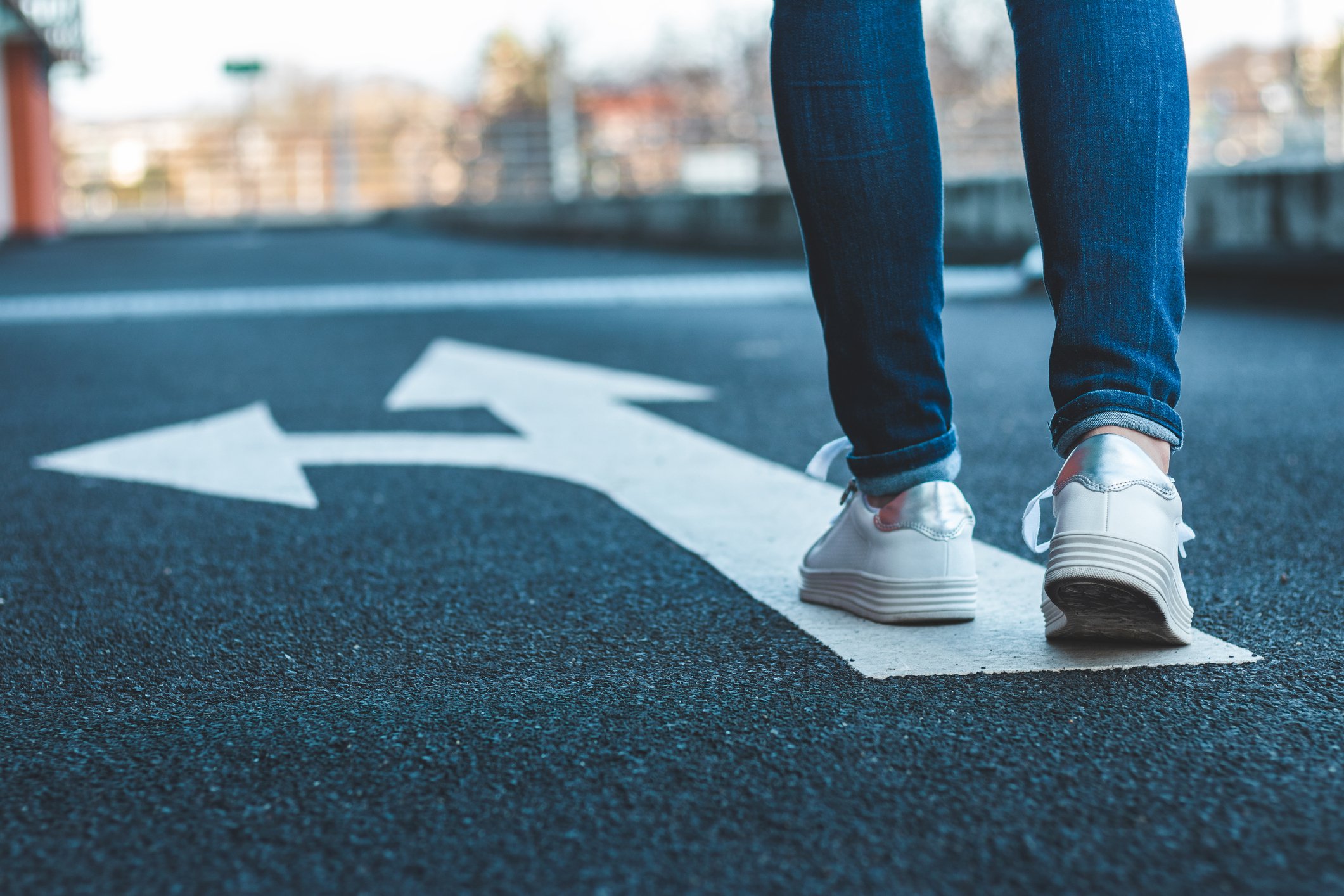 Pedestrian walking on road sign showing arrows pointing in different directions