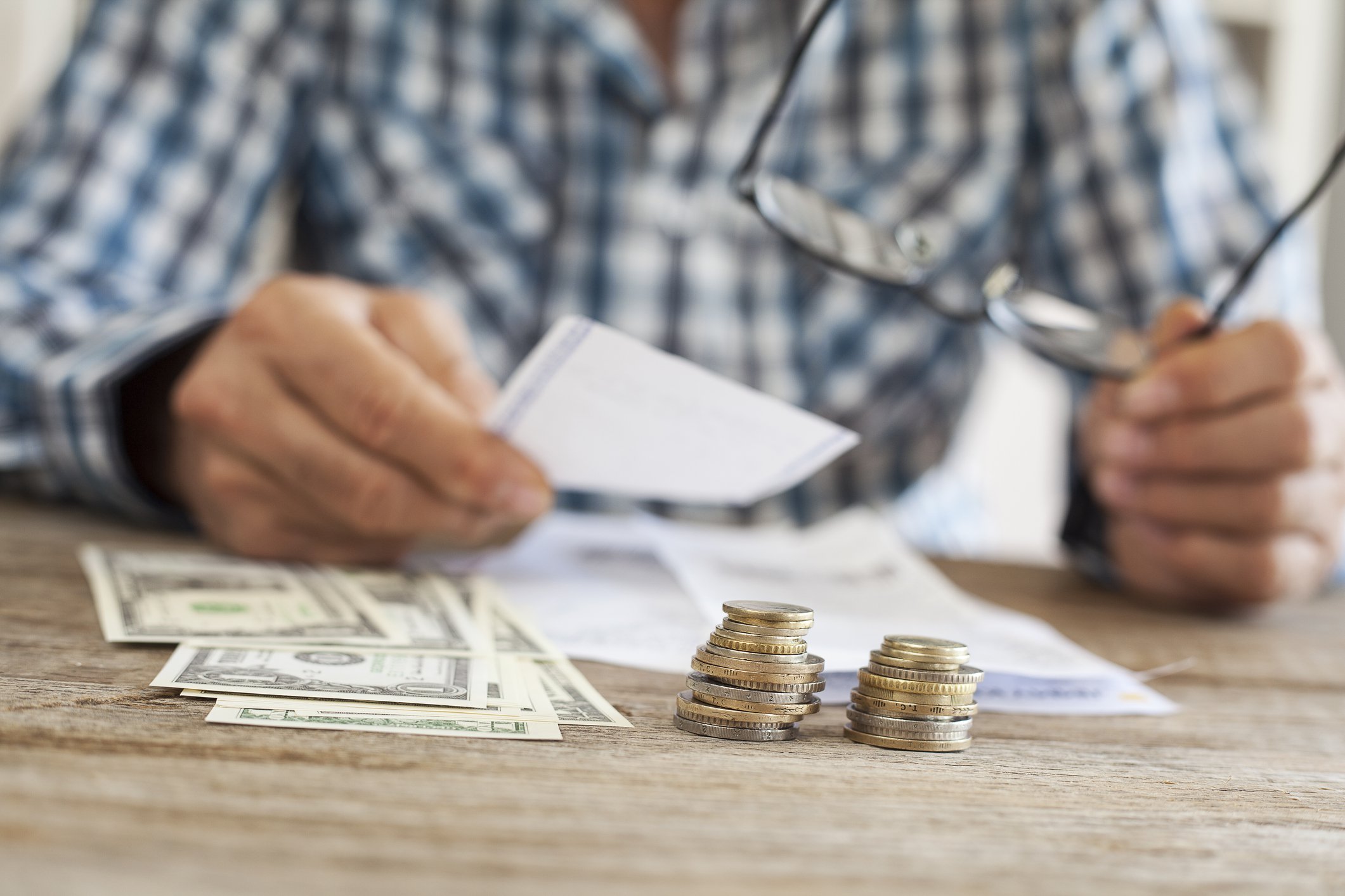 Man sorting paperwork on a table with dollars and coins sitting nearby.