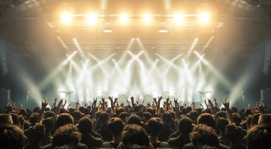 A crowd with hands in the air backlit by stage lights at a concert.