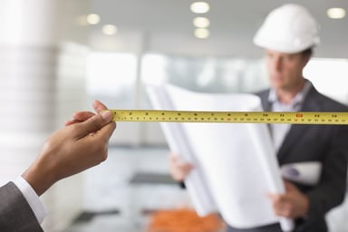 Construction workers inside a building with measuring tape and blueprint working on a store buildout