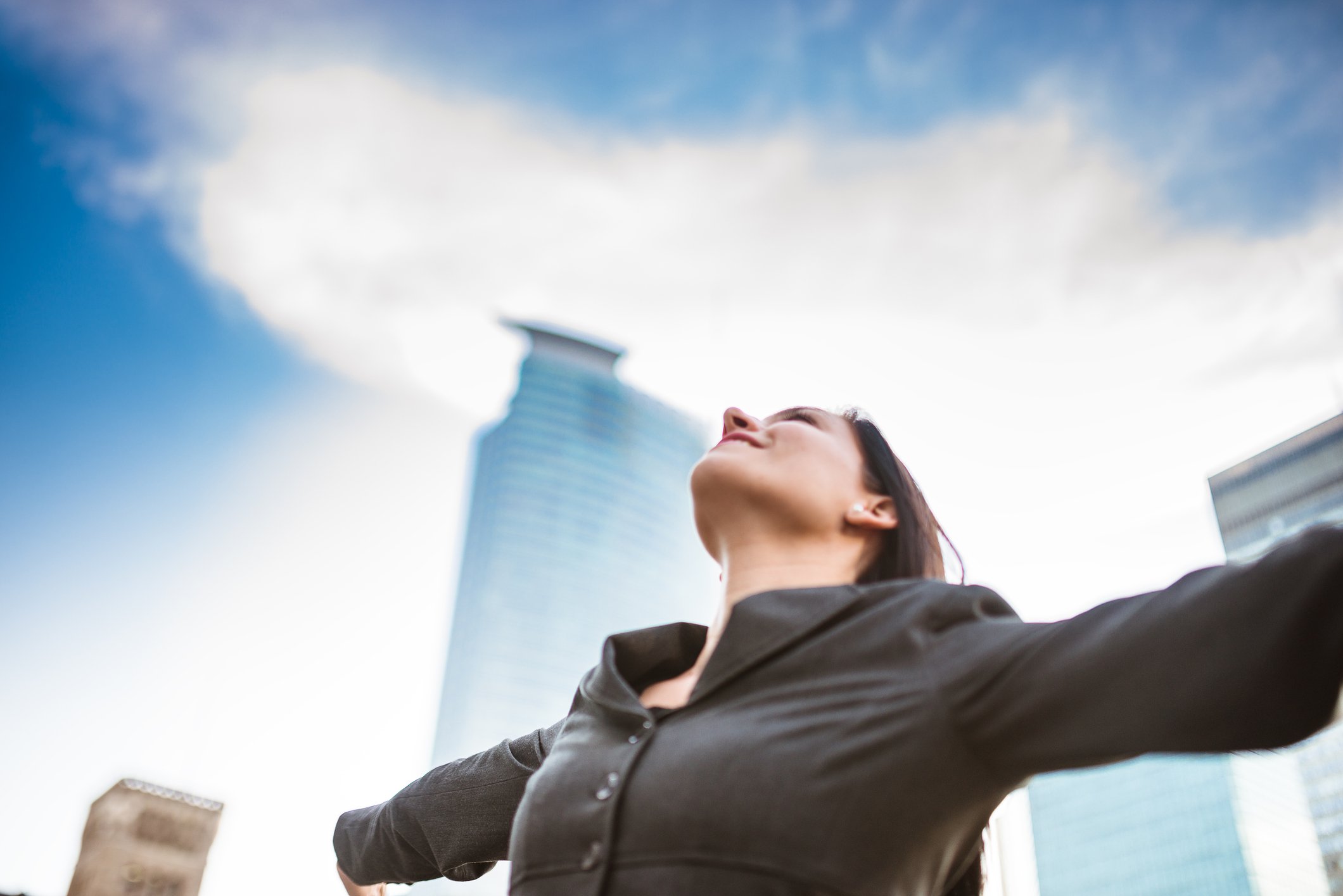 Woman spreads arms wide and looks up to sky.