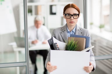 Young woman who just lost job carries a box of her personal belongings from office.