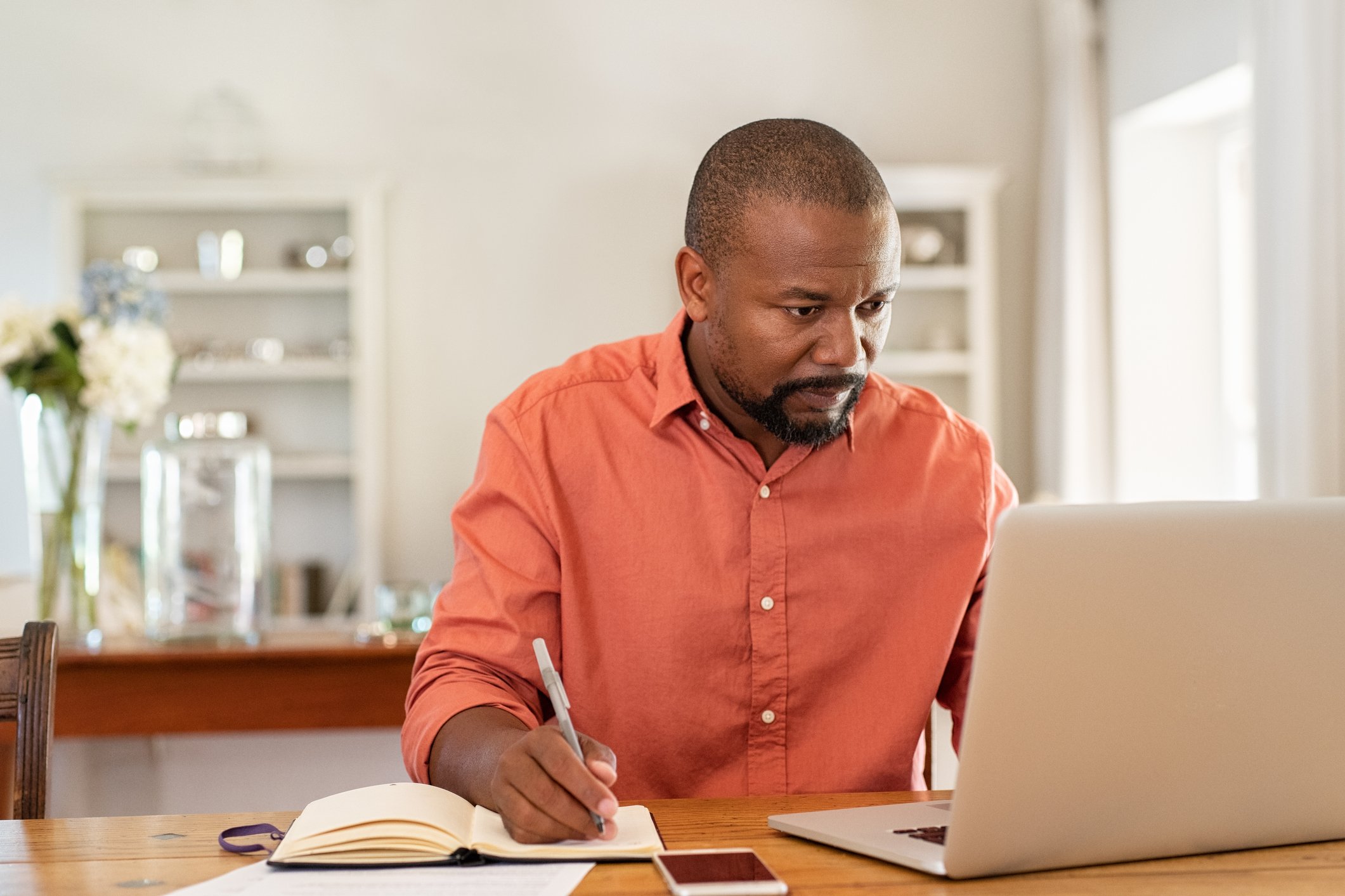 Man looking at computer and writing in book.