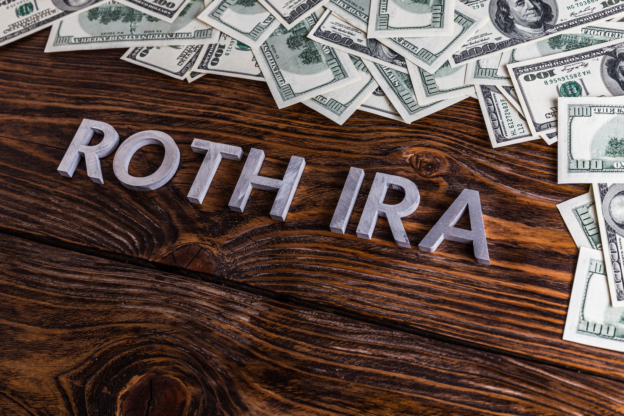 Silver letters spelling Roth IRA on floor with scattered hundred dollar bills