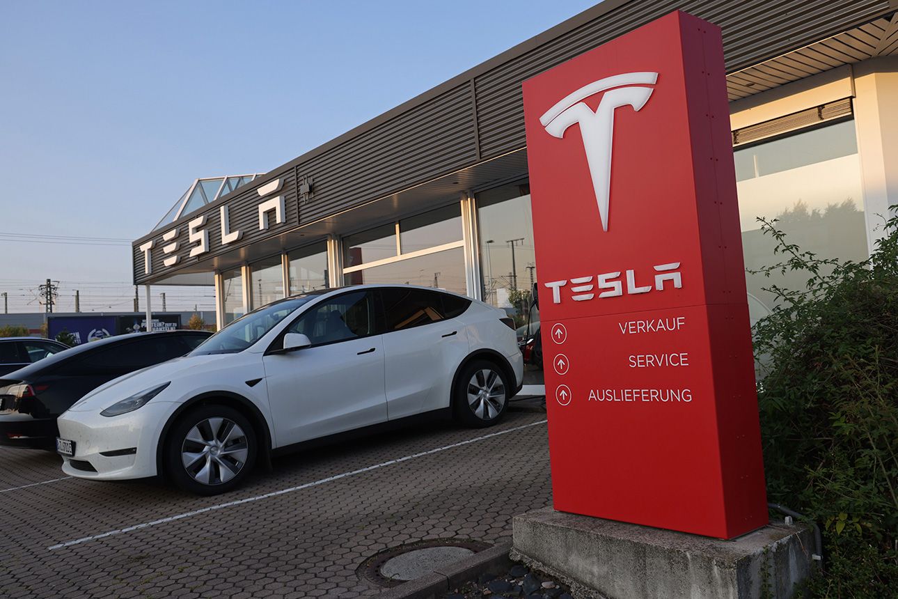 An all-electric Tesla Model Y SUV is parked in front of a Tesla dealership.