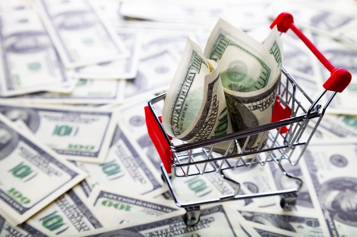 A hundred-dollar bill tucked into a mini shopping cart sitting on flattened hundreds.