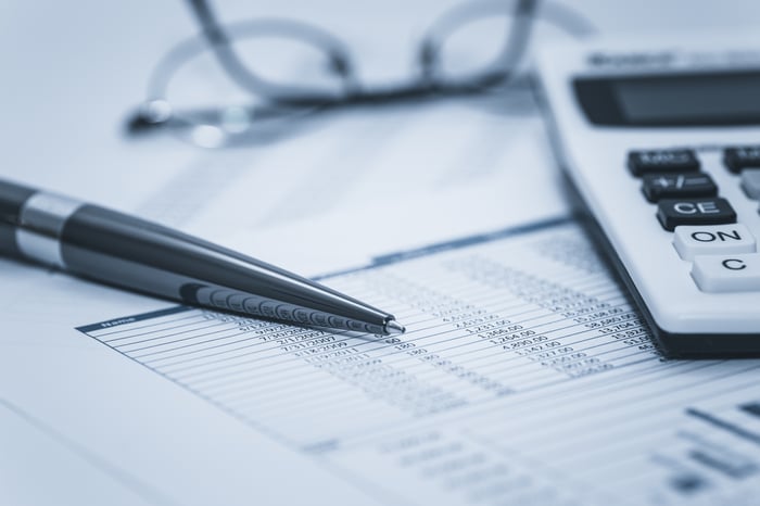 Spreadsheet with numbers lying under eyeglasses, a pen, and a calculator.