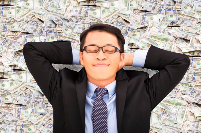 man in suit lying back on a bed of money, eyes closed, happy