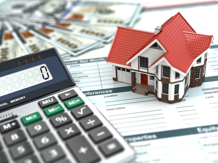 Money, model house, and calculator on top of paperwork