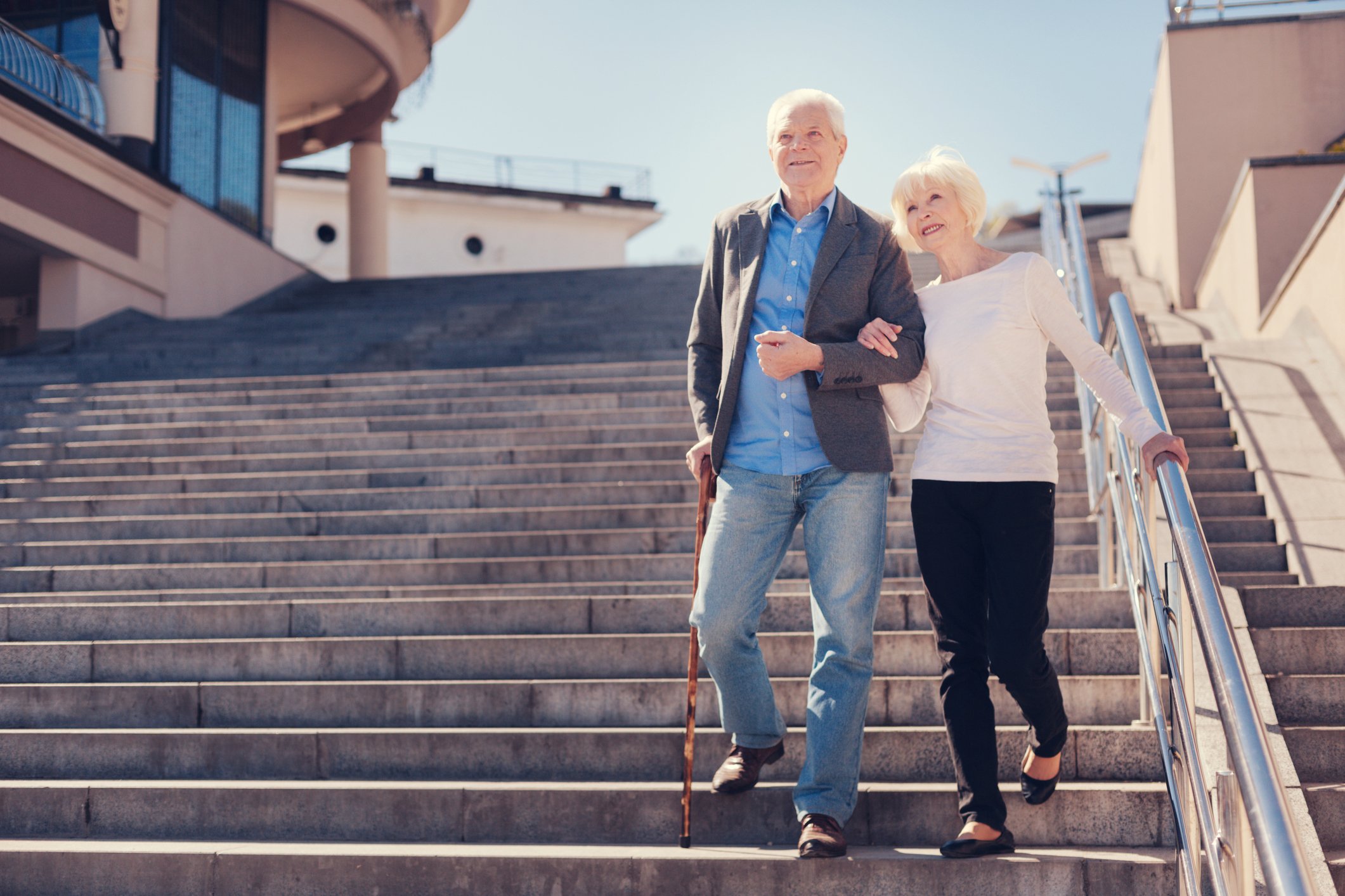 Happy elderly couple going down the stairs; the man is using a cane.