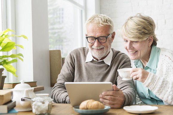 An older couple using a tablet together and enjoying tea.
