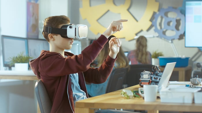 A person sitting at a desk using a virtual reality face mask.