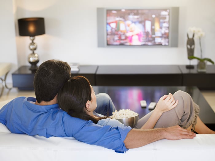 Couple sitting on couch watching TV, eating popcorn.