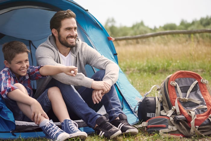 A man and his soon sit at the entrance to a tent in the woods