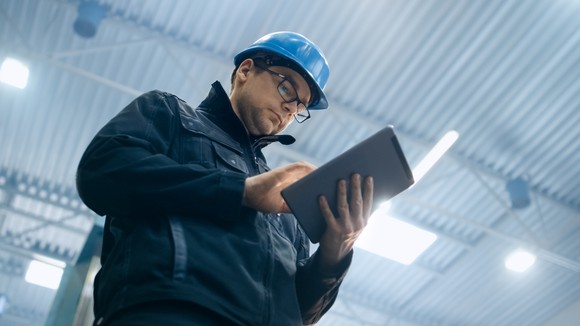 Man in construction hat, holding an iPad-type device