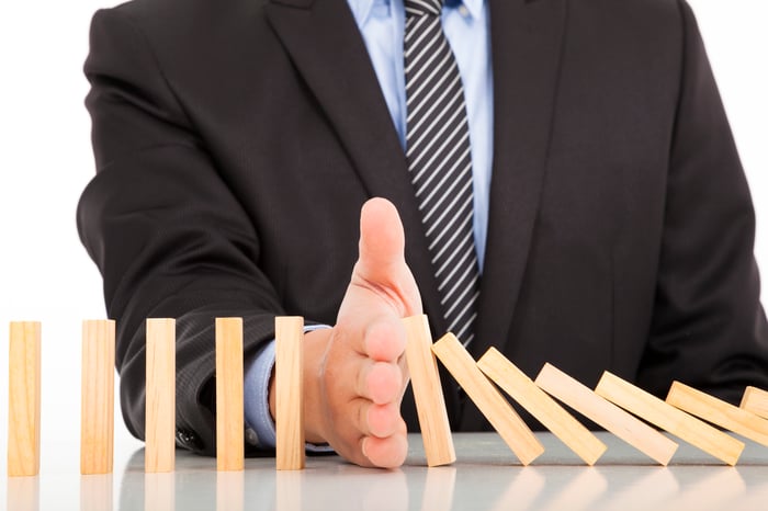 man's hand stopping dominoes from falling