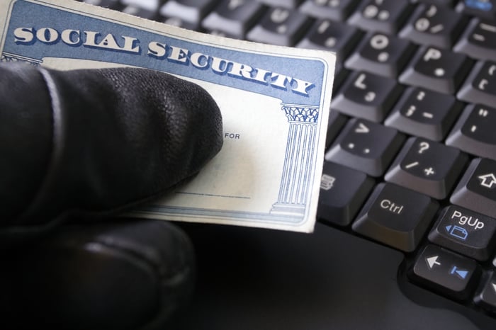 sinister gloved hand holding social security card over keyboard