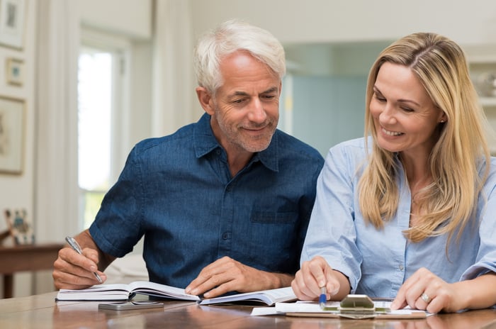 Mature couple discussing finances with pens and paper.