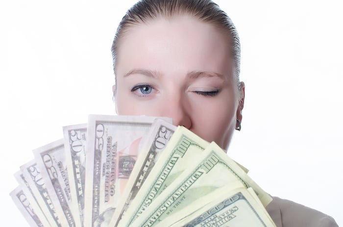 Woman holding lots of cash and winking.