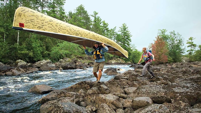 Man carrying a canoe overhead while walking beside a river