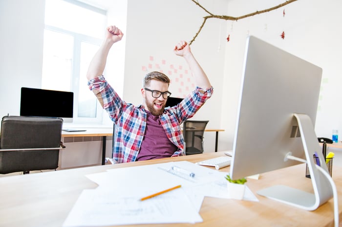 Guy raising fists in victory in front of computer