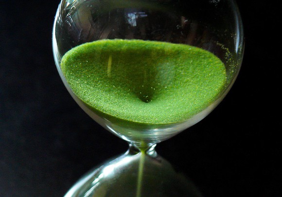 Hourglass with green sand falling through.