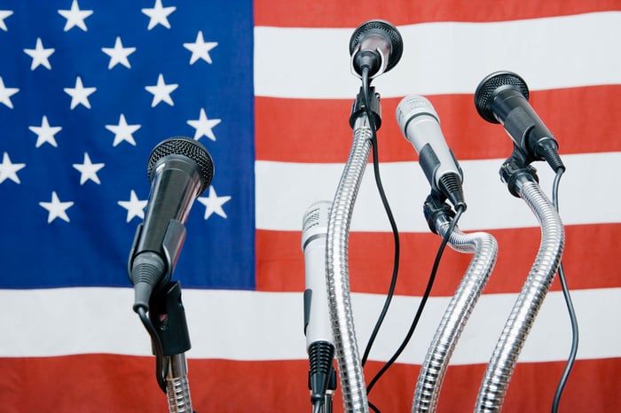 Microphones in front of an American flag - seemingly waiting for a politician to appear and speak