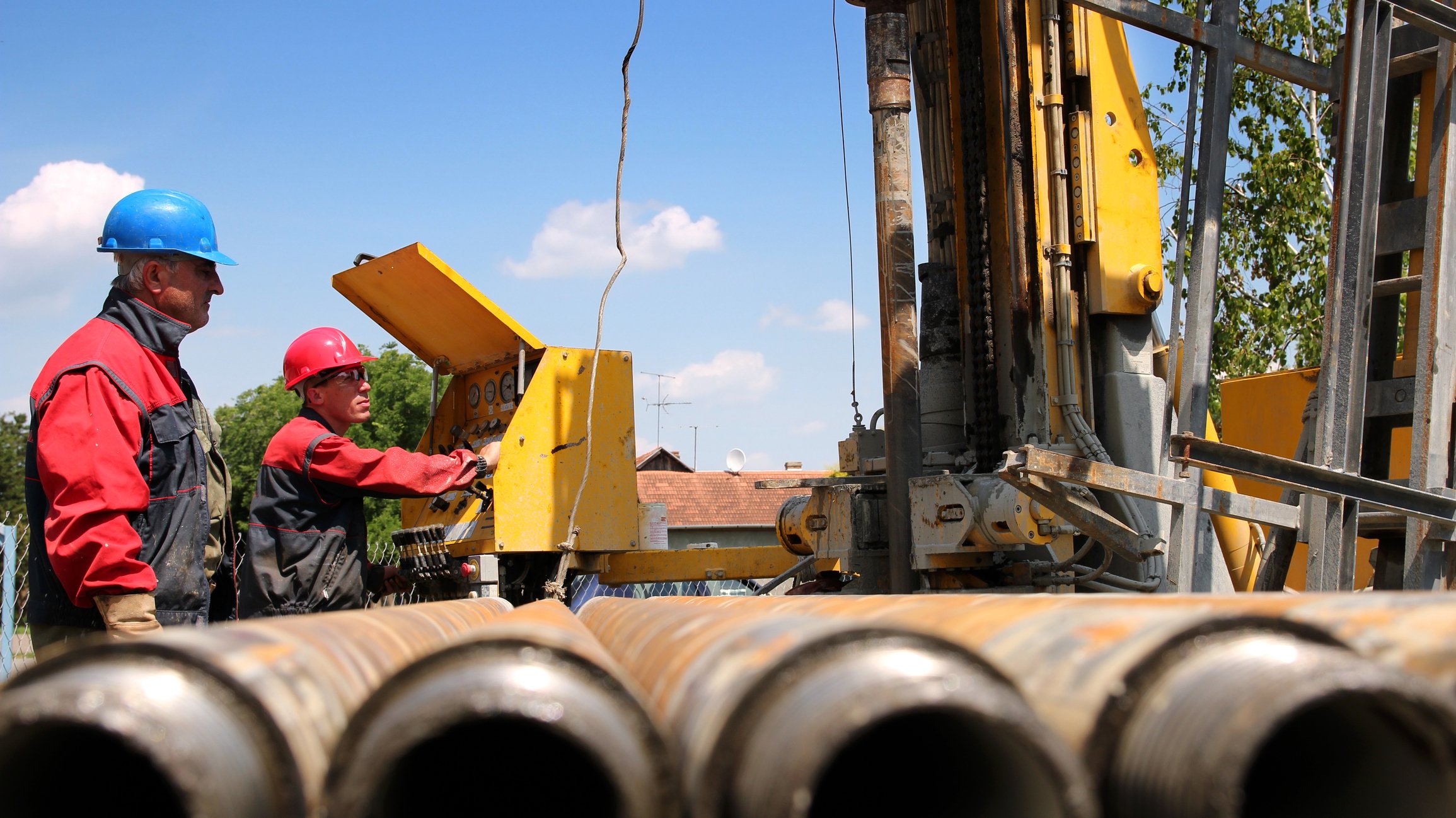 Oil field services workers with pipes and drilling rig