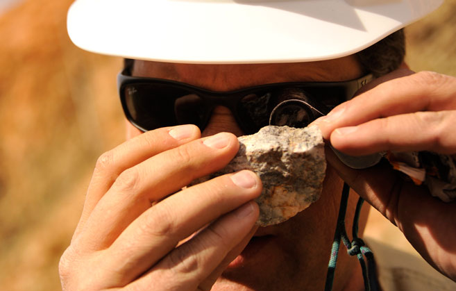 An image of a Hecla Mining employee examining a rock.