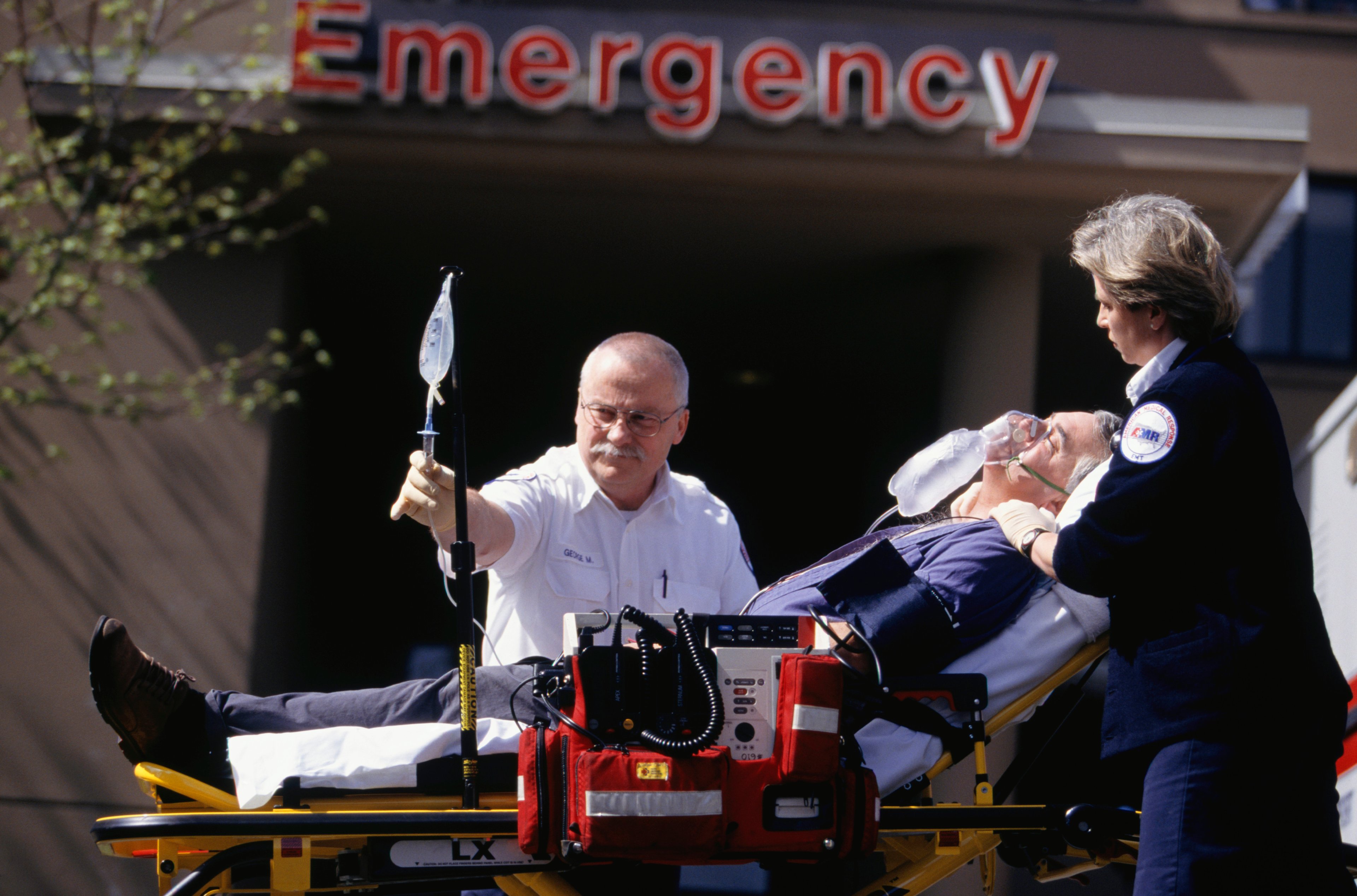 Ambulance workers transporting a sick patient in front of an emergency sign