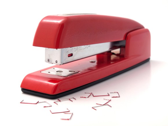 A red stapler with staples strewn alongside it.
