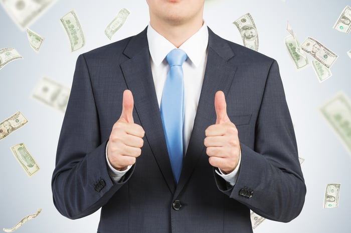 A businessman gives a thumbs-up with money in the background.