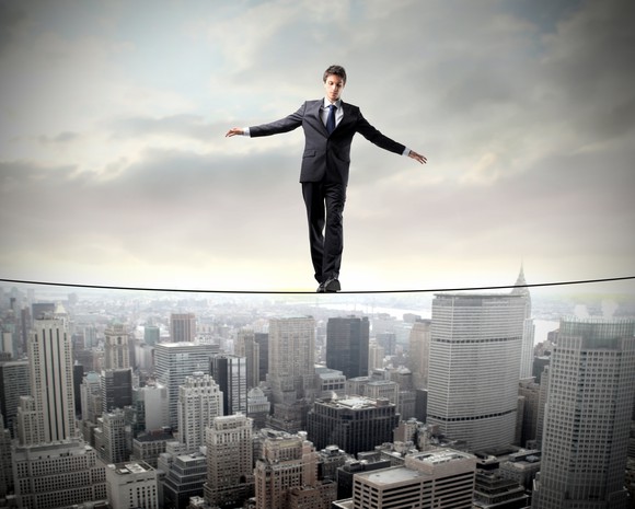 A businessman walks a high wire between two buildings.