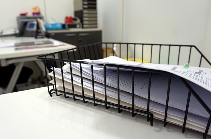 A pile of documents in a wire basket on a desk.