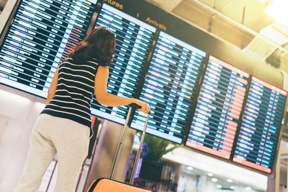 A woman looking at a large arrivals board at an airport.