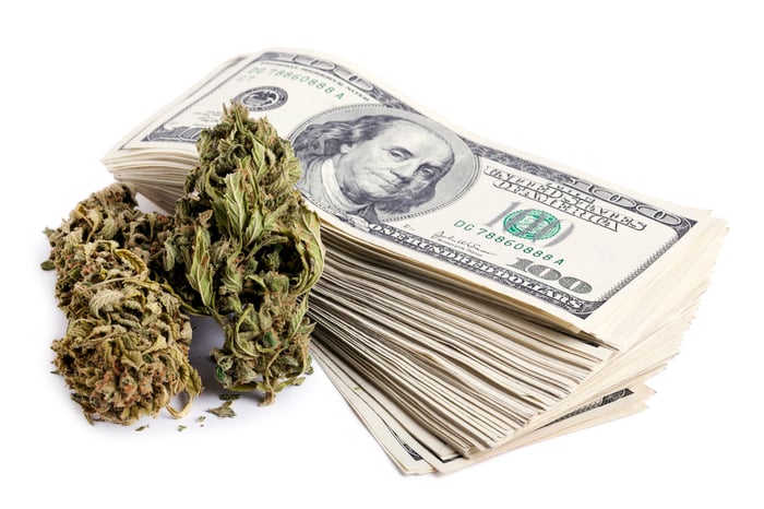 A marijuana bud next to a stack of hundred dollar bills.