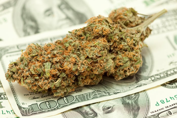 A marijuana bud sitting atop a pile of cash.