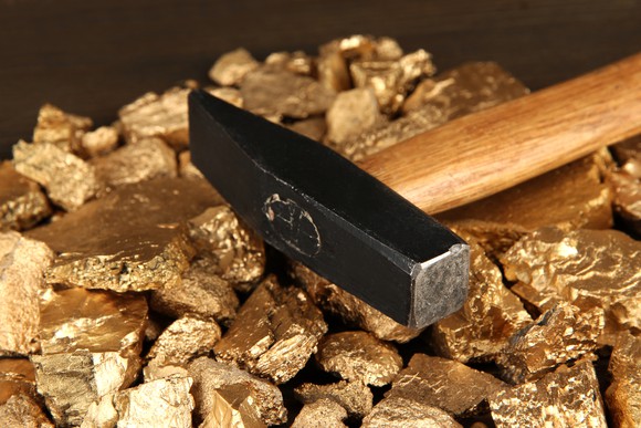 A pickaxe rests on a pile of gold nuggets.