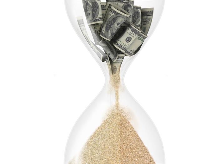 Money in an hourglass, turning into sand 