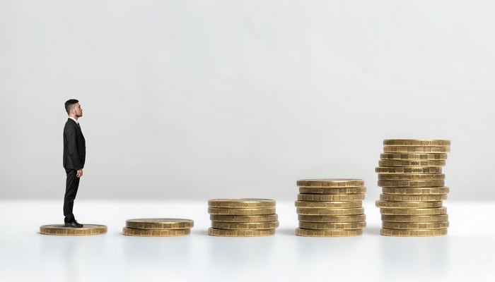 Man standing on a small stack of coins, looking at larger stacks ahead.