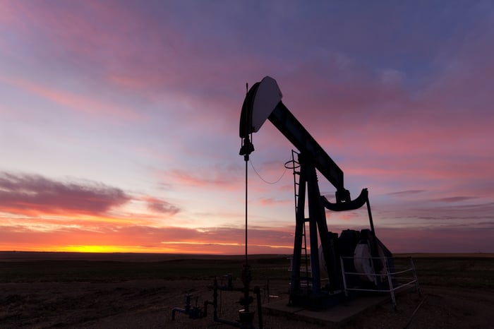 A close up photo of an oil well silhouette with a beautiful sunrise above the distant horizon.