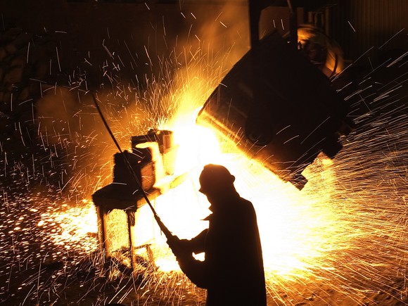 A steel worker in foundry, silhouetted against sparks flying behind him.