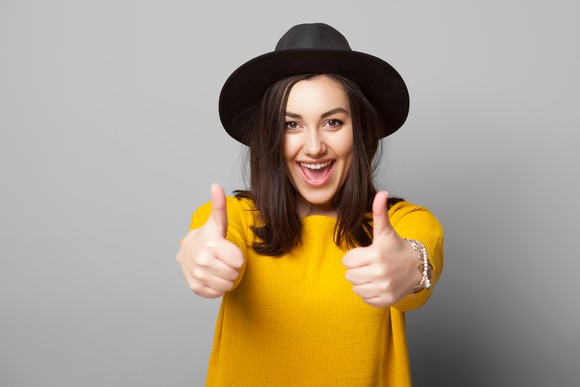 A young happy woman gives two thumbs up to the camera.
